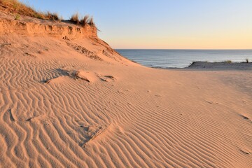 Coucher de soleil sur la côte atlantique française, à Soulac-sur-Mer. Les dunes sont striées par le vent. Le paysage est très coloré grâce à la lumière du soleil couchant et à l'océan. Tout est calme.