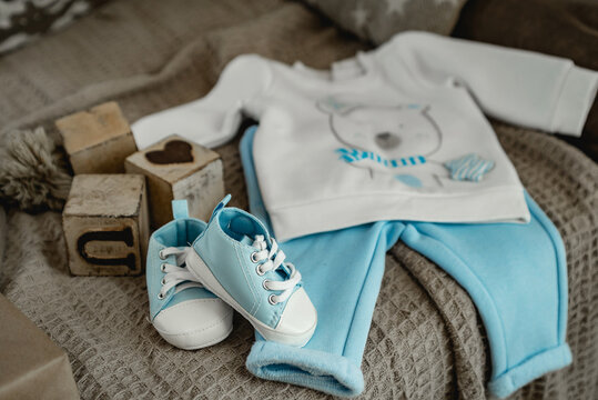 blue baby shoes and a blue suit on the bed next to the baby blocks