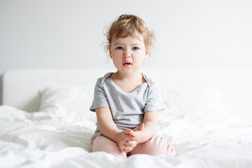 portrait of funny displeased cute little girl sitting on bed