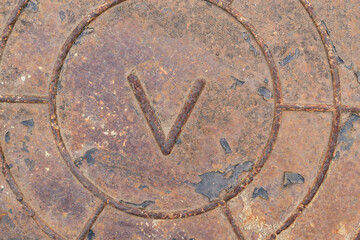 Old metal surface with latin letter V. Rust, scratches, remains of black leather. Concept of word Victory, military shield.