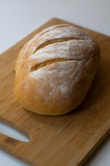 A loaf of homemade baked sourdough bread with three parallel cuts scoring on a wooden cutting board with a kitchen towel