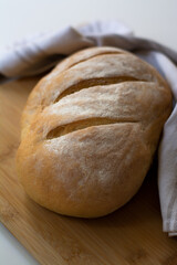 A loaf of homemade baked sourdough bread with three parallel cuts scoring on a wooden cutting board with a kitchen towel