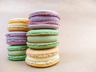 Multi-colored macaroons lie on a beige paper background. Orange, violet, green macaroon cakes on a light substrate. Background with macaroon. Tasty sweets on a light table.