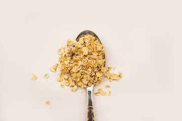 Oatmeal flakes in a metal spoon scattered on a white background. Dietary food. Healthy breakfast.Texture and background.