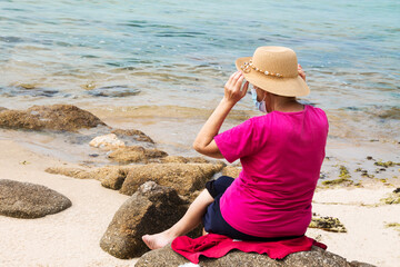 senior woman with hat and medical mask on the beach, prevention against viruses and infections