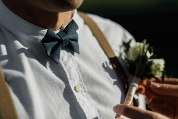 Groom in a white shirt with a bow tie and suspenders. elegant boutonniere