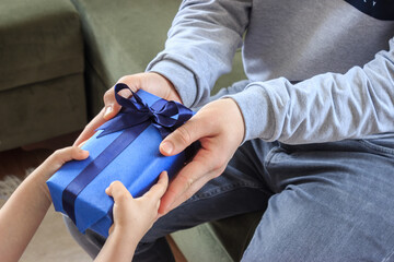 Loving childrLittle girl is giving a present to her dad. Caucasian father and daughter is holding blue gift box with hands. Father's day concept.en gifting father in living room
