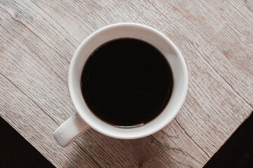 Top view of black coffee in white cup on wooden table. Brown tone photo