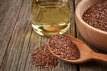 Flax seeds and a wooden spoon on a wooden table. Wooden bowl with bottle of oil. Healthy food and drink concept.