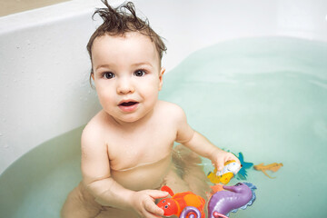 Cute happy little boy washing and playing in bathroom with colorful plastic toys. child's hygiene, healthy skin and body, happy lifestyle, carefree childhood concept