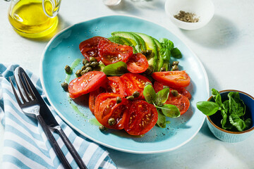 summer salad with ripe tomatoes and avocado with capers in a blue plate on the table