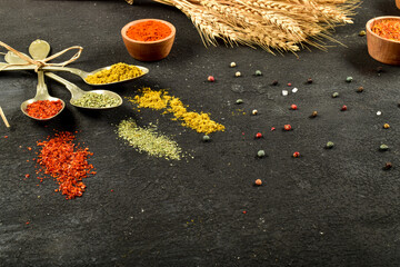 Top view of different kinds of colorful spices in spoons on black stone surface. Creative food concept texture with blank copy space for your message.