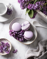 Purple macaroons with lilac flowers on a light marble background, top view. 
