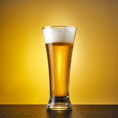 Cold craft light Beer in a glass with drops on a dark table. Pint of Beer on yellow color background.