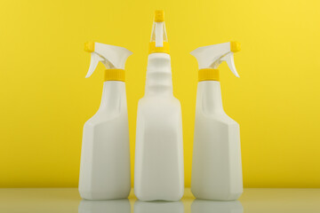 cleaning products in white spray bottles on yellow background 