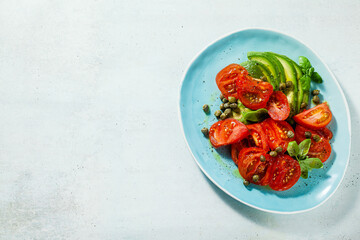 summer salad with ripe tomatoes and avocado with capers in a blue plate on the table