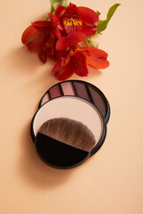 Fototapeta premium powder with professional face makeup brush and eyeshadows with flowers on beige background, close view, beauty concept 