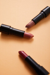 professional face makeup lipsticks on beige background, close view, beauty concept 