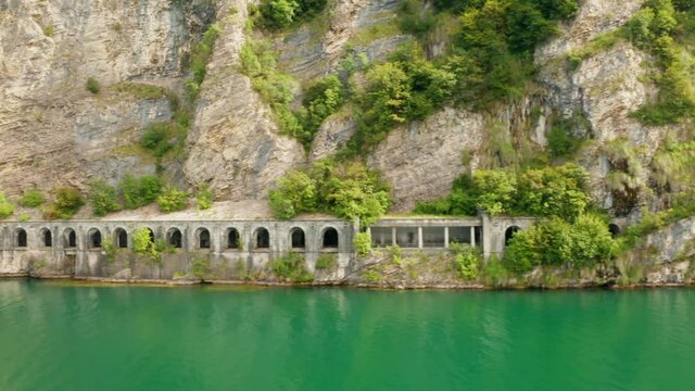 Aerial footage of tunnel Grumo in a rock along Lake Como with green water. Flight above Como Lake near the road, Italy