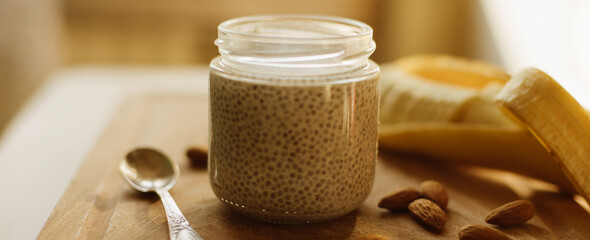 Dessert bowl of tasty chia seed pudding and banana, almond on wooden table on white background. Banner for website