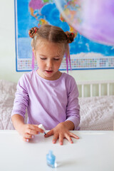 Little pretty girl paints herself nails with varnish