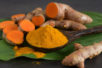 Turmeric powder in a black wooden spoon,leaves and fresh turmeric (curcumin) on black background,Is herbs and spices.