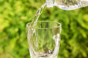 Pouring drinking water from bottle into glass on blurred green nature background