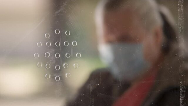 A woman wearing a medical mask speaks through holes in a plexiglass window at a charity food bank during the COVID-19 pandemic