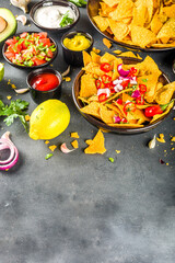 Nachos chips with melted cheese and various traditional mexican dips, salsa and jalapeno, dark grey background top view copy space