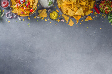 Nachos chips with melted cheese and various traditional mexican dips, salsa and jalapeno, dark grey...