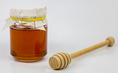 Glass jar with honey and a wooden stick on a white background