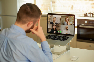 Back view of a male employee who works remotely listening to his colleagues about business in a video conference on a laptop computer at home. A multiethnic business team at an online meeting.