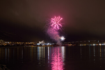 Beautiful firework on night sky in tromsoe city with bridge, cathedral and colorful reflection on the cold fjord water surface on new years eve