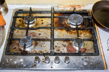 A scruffy and dirty kitchen, a stove in grease, in the sink a mountain of unwashed dishes....