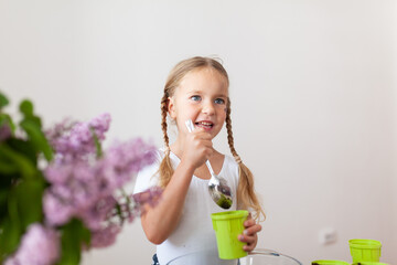 Little girl in a white T-shirt plants pea seeds in green pots, a child cares for plants, a home garden on the window
