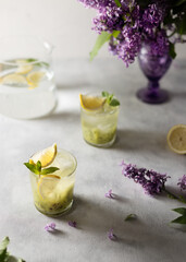 Fresh summer lemonnad with mint and kiwi stands on the table. Nearby is a bouquet of lilacs in a purple vase.