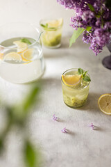 Fresh summer lemonnad with mint and kiwi stands on the table. Nearby is a bouquet of lilacs in a purple vase.