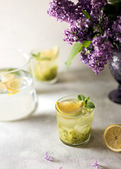Fresh summer lemonnad with mint and kiwi stands on the table. Nearby is a bouquet of lilacs in a purple vase.