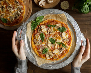 Flat lay with homemade italian pizza, olive oil, tomatoes, meat and cheese on wooden brown table.