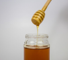 Glass jar with honey and a wooden stick on a white background. Pouring aromatic honey into jar, closeup.