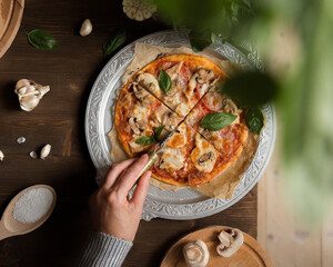 Flat lay with homemade italian pizza, olive oil, tomatoes, meat and cheese on wooden brown table.