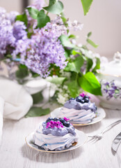 Obraz na płótnie Canvas Porcelain plate with meringue with whipped cream decorated with lilac flowers on wooden background
