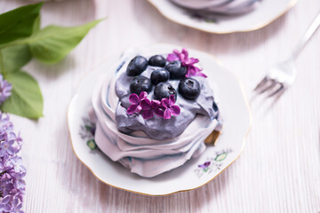 Porcelain plate with meringue with whipped cream decorated with lilac flowers on wooden background