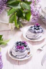 Porcelain plate with meringue with whipped cream decorated with lilac flowers on wooden background
