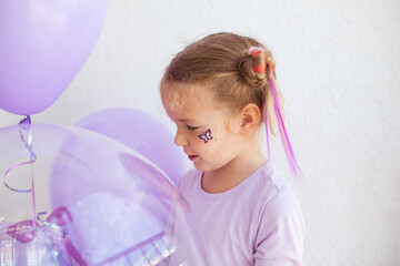 Portrait of a cheerful pretty girl with purple and transparent balloons, a holiday at the child