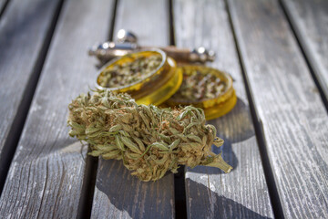 Wood table with marijuana grinder, marijuana bud and a smoking pipe.