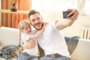 Father and daughter. Handsome young man and little cute girl make funny selfie on smartphone at home, have fun. Dad and child laugh. Father's day.