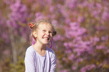 Portrait of a happy cheerful little girl in a purple dress on a background of blooming purple trees, a child walk in the garden with blooming cherries