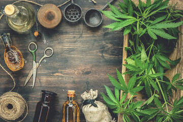 Cannabis CBD oil bottles and green plant leaves on dirty wooden table background.