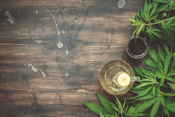 Cannabis CBD oil bottles and green plant leaves on dirty wooden table background.